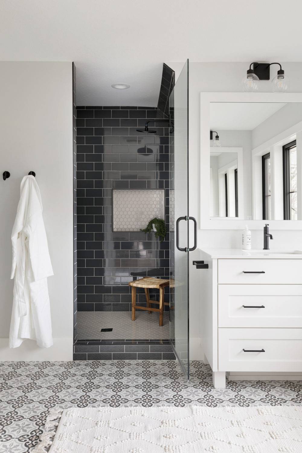 Black and white bathroom with patterned tile flooring and black subway tile shower