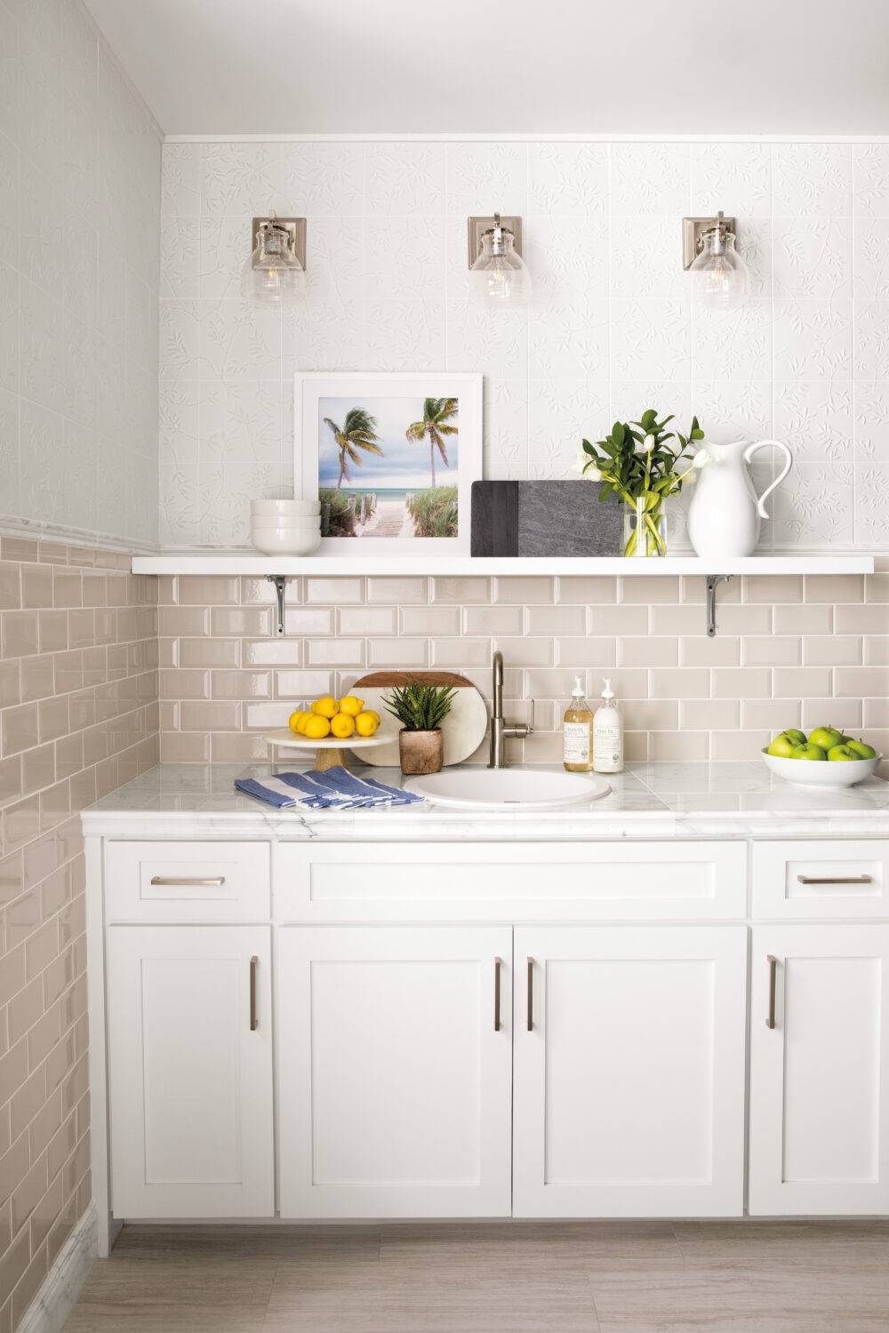 Kitchen backsplash using a white gloss tile set vertically in a picket shape. Counter is beige on white cabinets with black hardware.